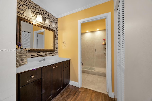 bathroom featuring decorative backsplash, hardwood / wood-style flooring, ornamental molding, vanity, and tiled shower