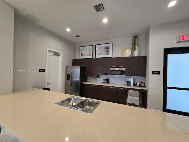 kitchen featuring tasteful backsplash, sink, dark brown cabinetry, kitchen peninsula, and stainless steel appliances