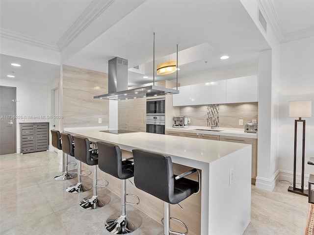 kitchen featuring a breakfast bar area, crown molding, island range hood, hanging light fixtures, and white cabinets