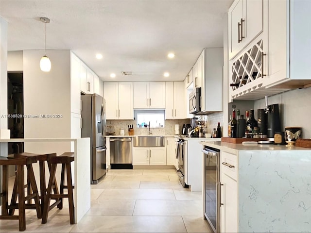 kitchen featuring pendant lighting, sink, stainless steel appliances, white cabinets, and beverage cooler