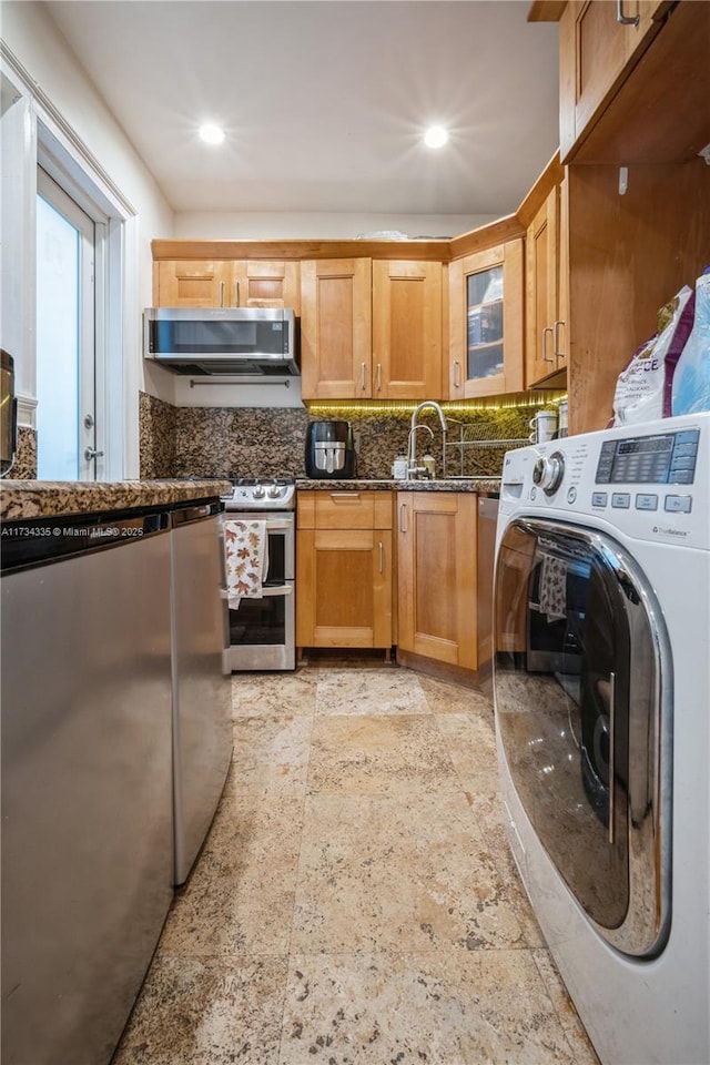 kitchen with sink, tasteful backsplash, dark stone countertops, appliances with stainless steel finishes, and washer / clothes dryer