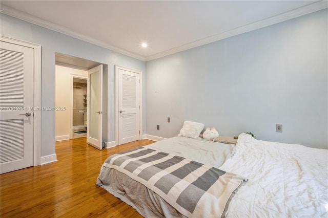 bedroom featuring wood-type flooring, ornamental molding, and multiple closets