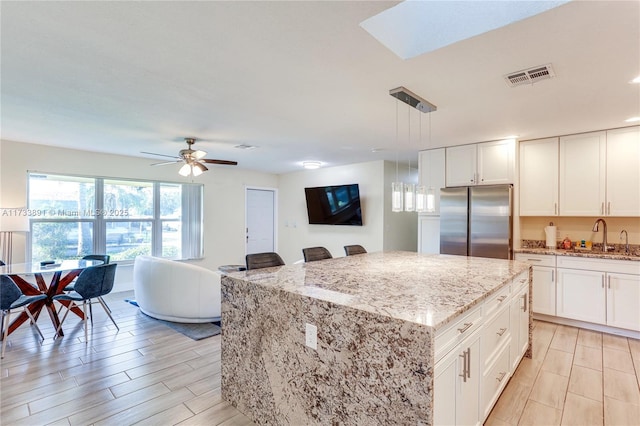 kitchen with a kitchen island, pendant lighting, sink, stainless steel fridge, and light stone countertops