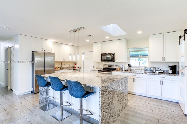 kitchen with white cabinetry, hanging light fixtures, a center island, stainless steel appliances, and light stone countertops