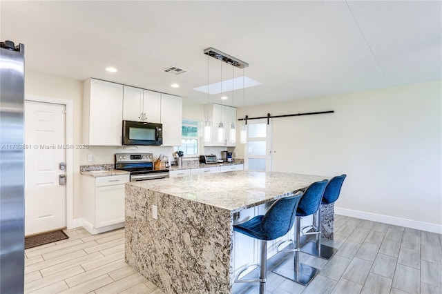 kitchen featuring appliances with stainless steel finishes, decorative light fixtures, white cabinetry, a center island, and a barn door