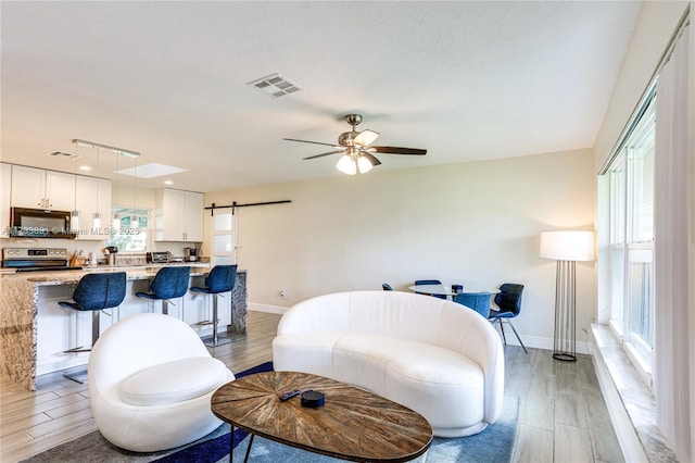 living room with ceiling fan, a barn door, a textured ceiling, and light hardwood / wood-style floors