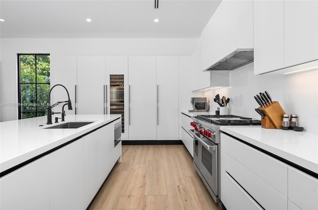 kitchen with range hood, sink, white cabinets, double oven range, and light wood-type flooring