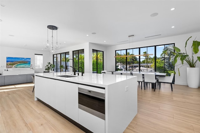 kitchen with sink, decorative light fixtures, a center island with sink, wall oven, and white cabinets