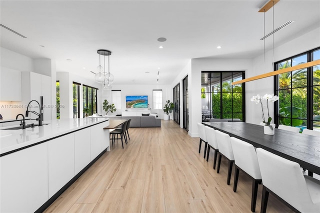 kitchen with sink, white cabinetry, light hardwood / wood-style flooring, hanging light fixtures, and a notable chandelier