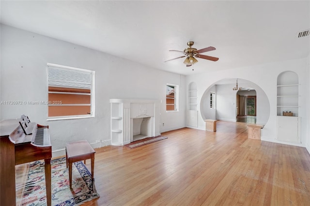 living room with ceiling fan, built in features, and light wood-type flooring