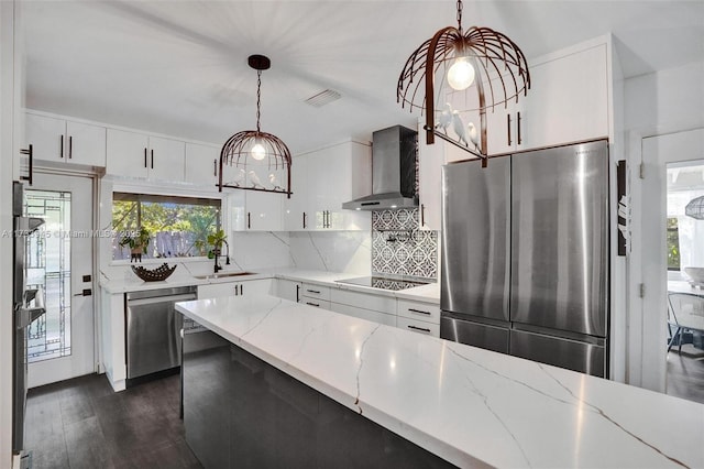 kitchen with white cabinets, wall chimney range hood, appliances with stainless steel finishes, and pendant lighting