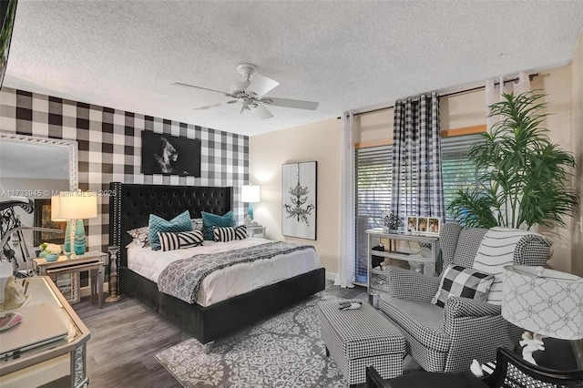 bedroom with an accent wall, ceiling fan, a textured ceiling, wood finished floors, and wallpapered walls