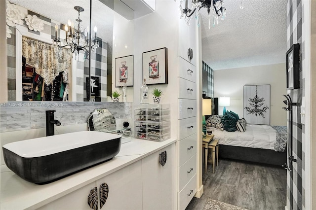 ensuite bathroom featuring a textured ceiling, connected bathroom, wood finished floors, a sink, and decorative backsplash