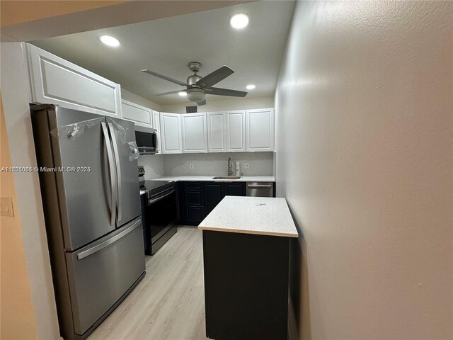 kitchen featuring appliances with stainless steel finishes, white cabinetry, sink, a center island, and light wood-type flooring