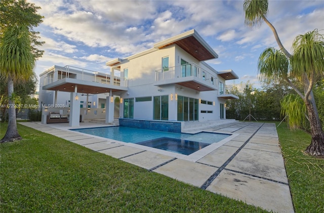 rear view of house featuring a swimming pool with hot tub, a balcony, a yard, and a patio area