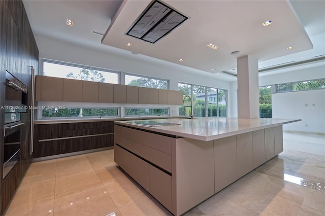 kitchen with black electric cooktop, light tile patterned floors, sink, and a large island with sink