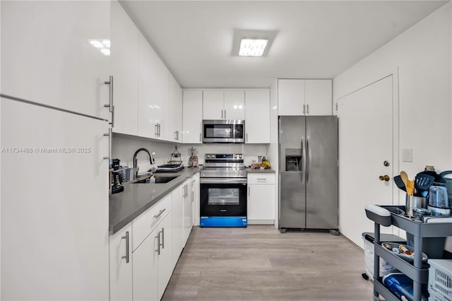 kitchen with stainless steel appliances, dark countertops, light wood-style flooring, white cabinets, and a sink