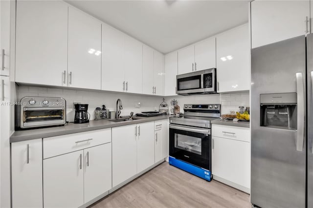 kitchen featuring light wood-type flooring, appliances with stainless steel finishes, white cabinets, and a sink