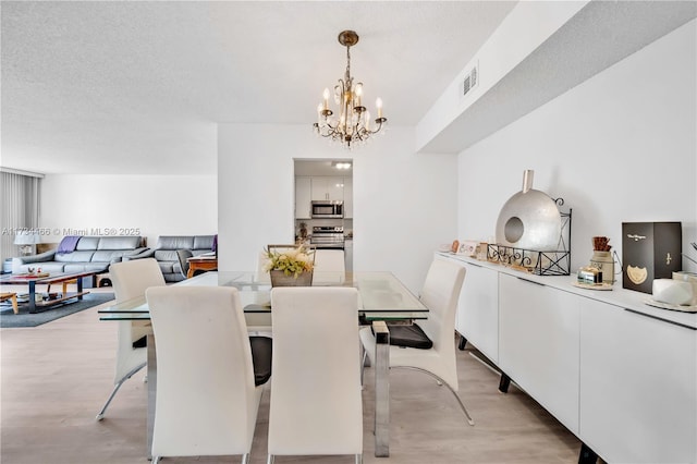 dining space with visible vents, light wood-style flooring, a textured ceiling, and an inviting chandelier