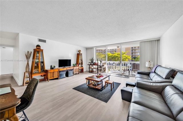 living room featuring a textured ceiling, floor to ceiling windows, visible vents, and wood finished floors