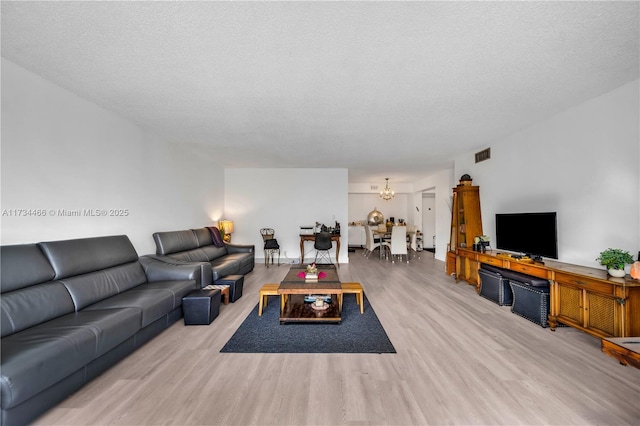 living room with an inviting chandelier, a textured ceiling, visible vents, and wood finished floors