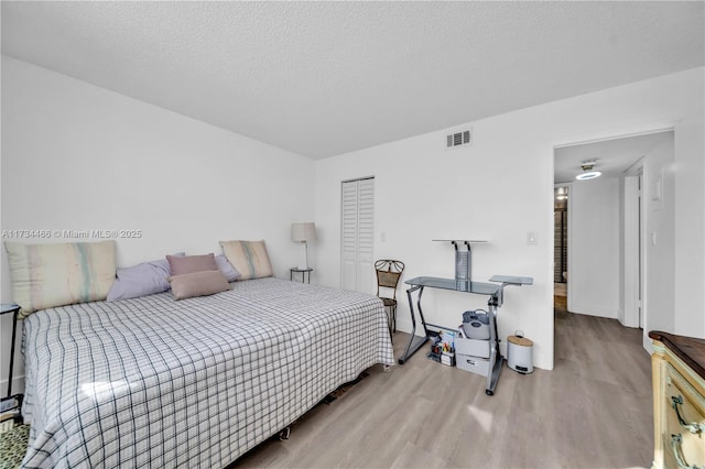 bedroom with visible vents, a textured ceiling, and wood finished floors