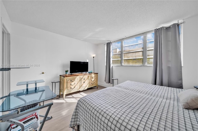 bedroom with a textured ceiling, baseboards, and wood finished floors