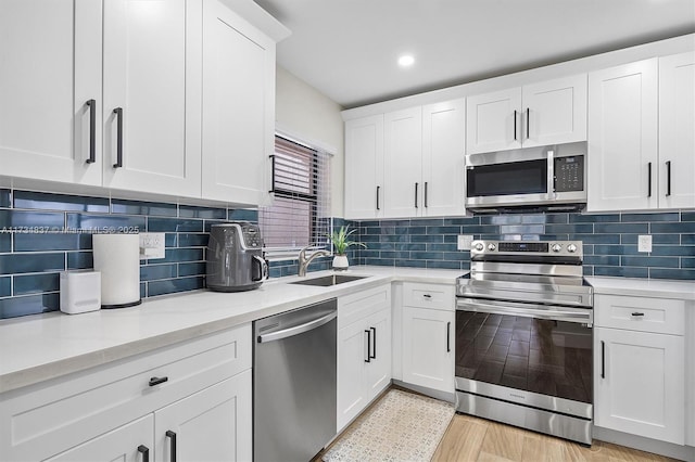 kitchen featuring sink, appliances with stainless steel finishes, white cabinetry, light stone countertops, and decorative backsplash