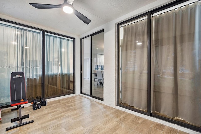 exercise area featuring ceiling fan, light hardwood / wood-style flooring, and a textured ceiling