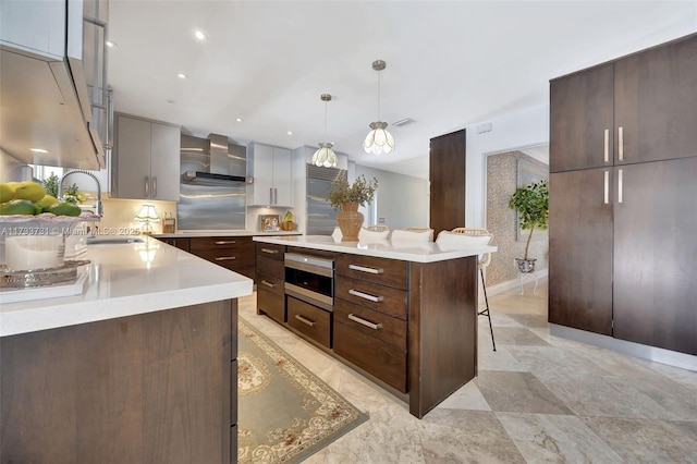 kitchen featuring sink, a breakfast bar area, a center island, pendant lighting, and wall chimney range hood