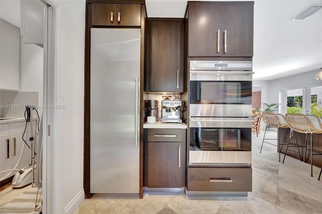 kitchen with stainless steel appliances, light tile patterned flooring, and dark brown cabinets