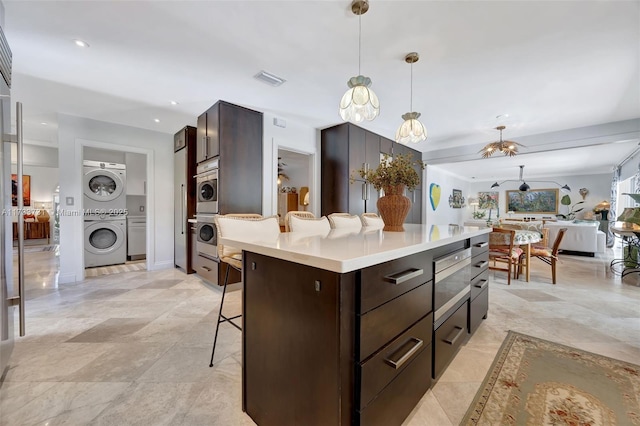 kitchen with stacked washer and dryer, a breakfast bar, dark brown cabinets, a kitchen island, and pendant lighting