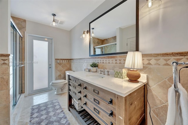 bathroom with tile walls, vanity, toilet, and an enclosed shower