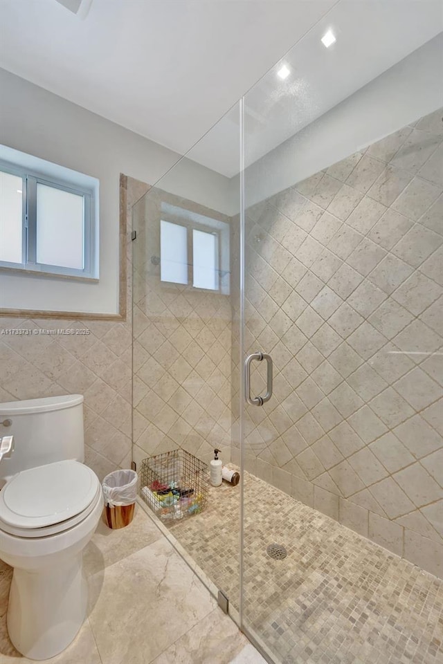 bathroom with toilet, tile walls, and a shower with shower door