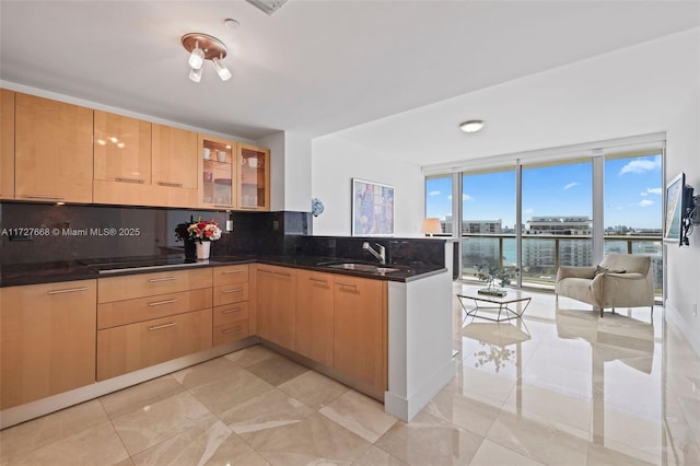 kitchen featuring sink, backsplash, dark stone counters, kitchen peninsula, and light brown cabinets