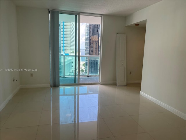 tiled empty room featuring a wall of windows and a textured ceiling