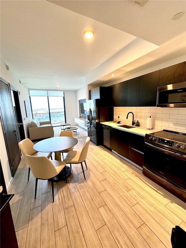 kitchen featuring floor to ceiling windows, sink, light hardwood / wood-style floors, decorative backsplash, and black appliances