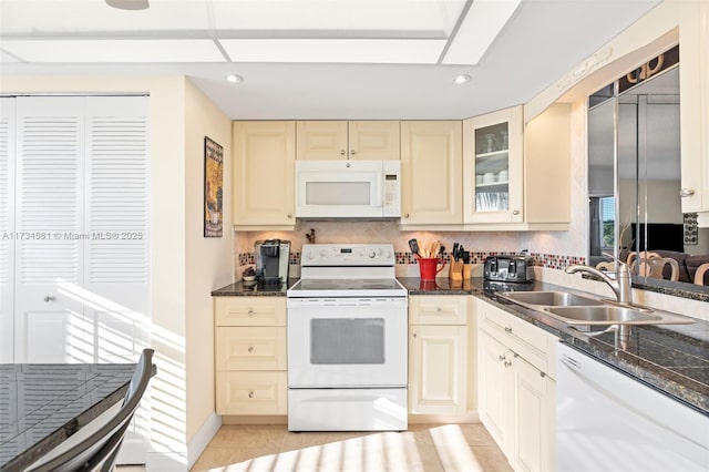 kitchen featuring sink, white appliances, dark stone counters, cream cabinets, and backsplash