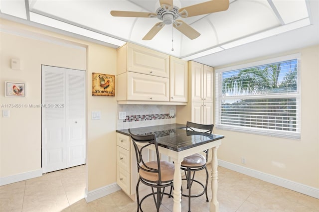 kitchen featuring light tile patterned flooring, backsplash, a kitchen breakfast bar, ceiling fan, and cream cabinetry