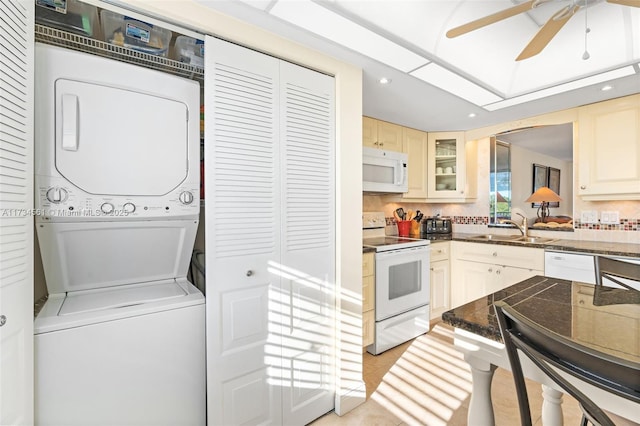 kitchen featuring sink, white appliances, backsplash, stacked washer / dryer, and cream cabinetry