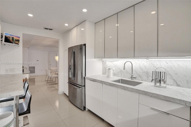 kitchen featuring sink, stainless steel fridge, backsplash, white cabinets, and light tile patterned flooring