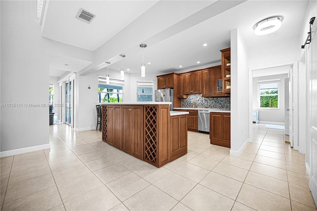 kitchen with appliances with stainless steel finishes, pendant lighting, backsplash, a center island, and light tile patterned floors