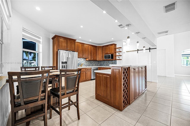 kitchen featuring appliances with stainless steel finishes, decorative light fixtures, tasteful backsplash, a center island, and a barn door