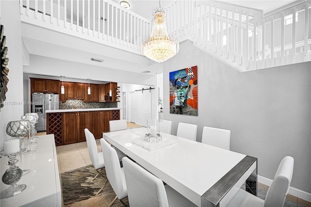 dining room with light tile patterned flooring, a barn door, a chandelier, and a high ceiling