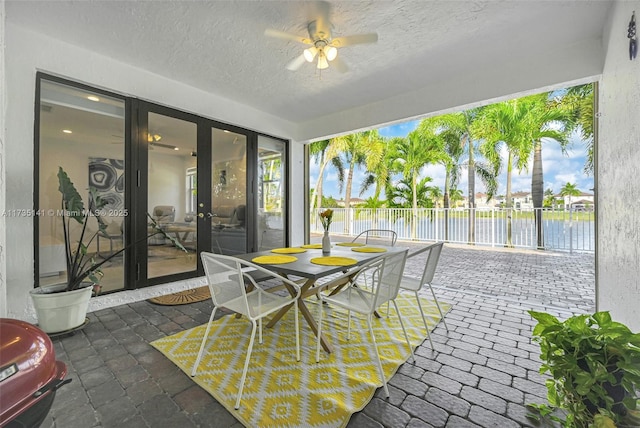 sunroom featuring ceiling fan and a water view