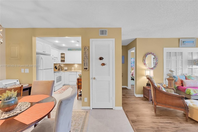 kitchen with white cabinetry, white appliances, a textured ceiling, and light wood-type flooring