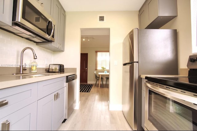 kitchen with gray cabinetry, decorative backsplash, light hardwood / wood-style flooring, and appliances with stainless steel finishes