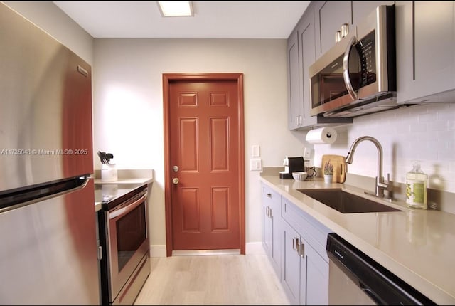 kitchen with gray cabinets, sink, backsplash, stainless steel appliances, and light hardwood / wood-style flooring