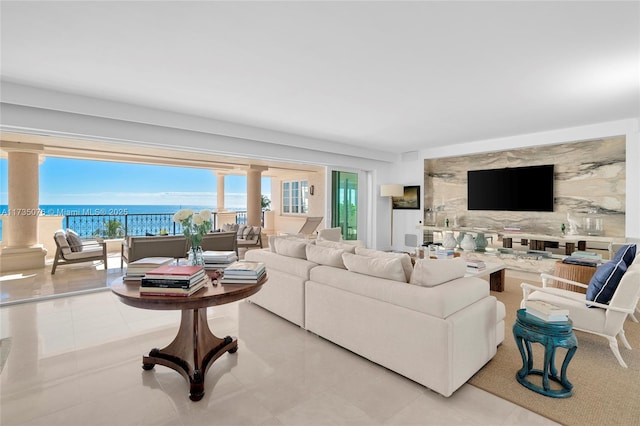 living room featuring light tile patterned flooring, a water view, and ornate columns