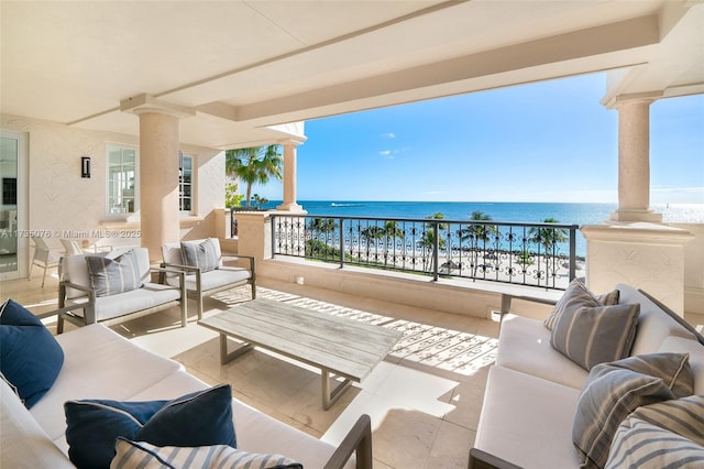 balcony with an outdoor living space, a water view, and a view of the beach